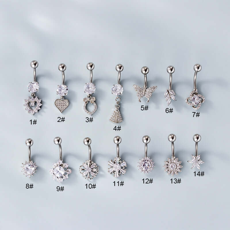 A set of silver belly rings with various embellishments, including a heart-shaped dangle, displayed on a flat surface.