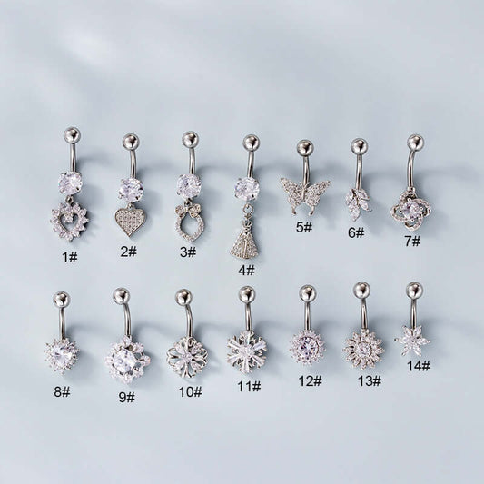 A set of silver belly rings with various embellishments, including a heart-shaped dangle, displayed on a flat surface.