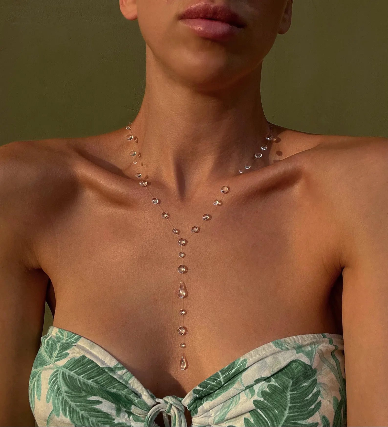 Woman wearing a green leaf-patterned strapless top with a necklace against a green background