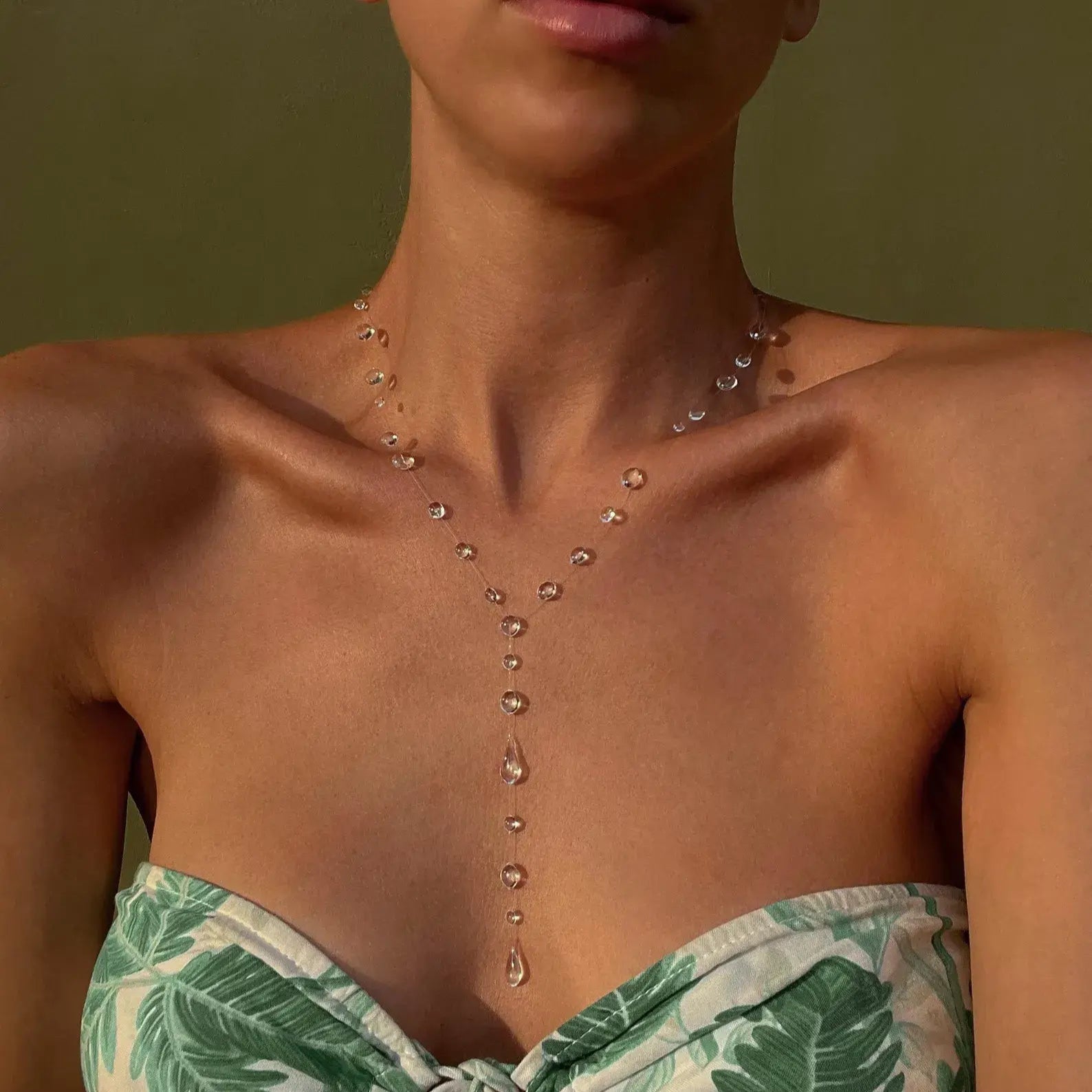 Woman wearing a green leaf-patterned strapless top with a necklace against a green background