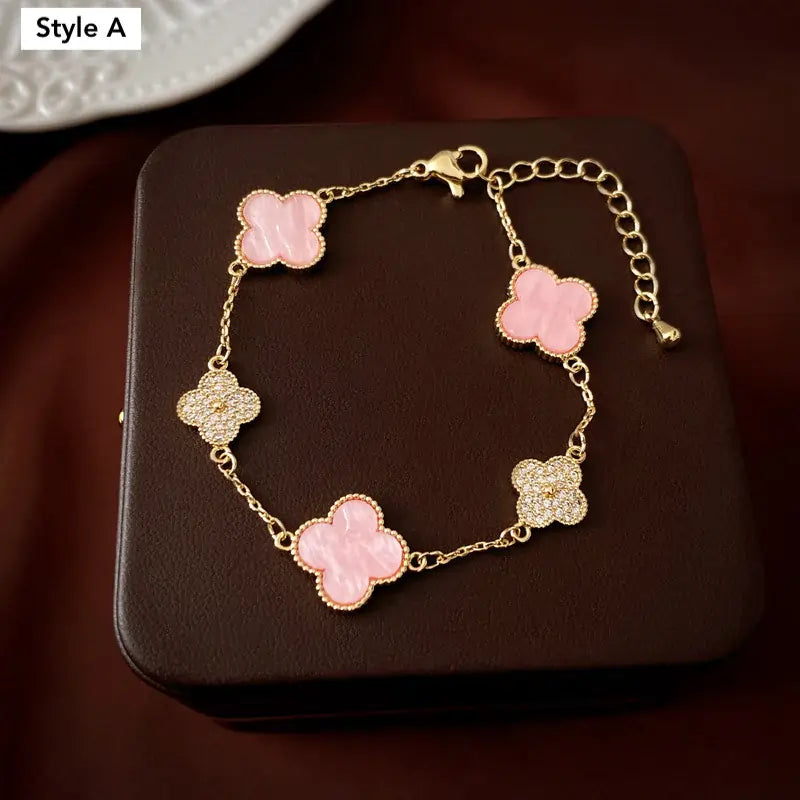 Gold bracelet with pink clover-shaped charms on a dark surface