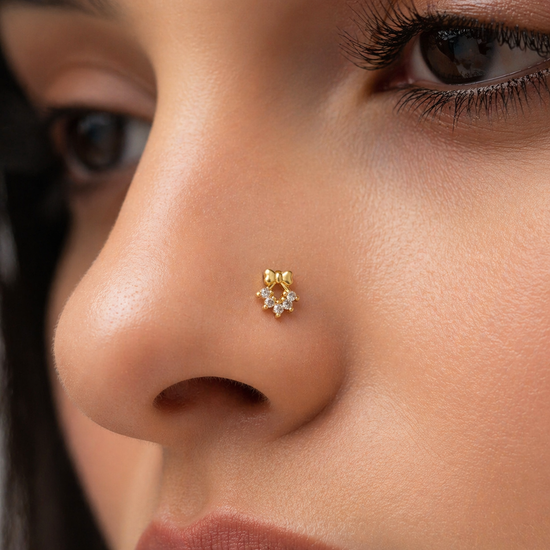 Close-up of a person wearing a gold bow nose ring with a small design.