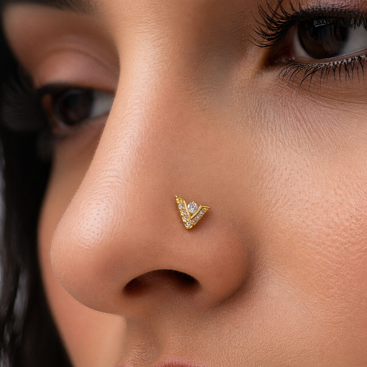 Close-up of a person wearing a v shaped gold nose ring with a diamond