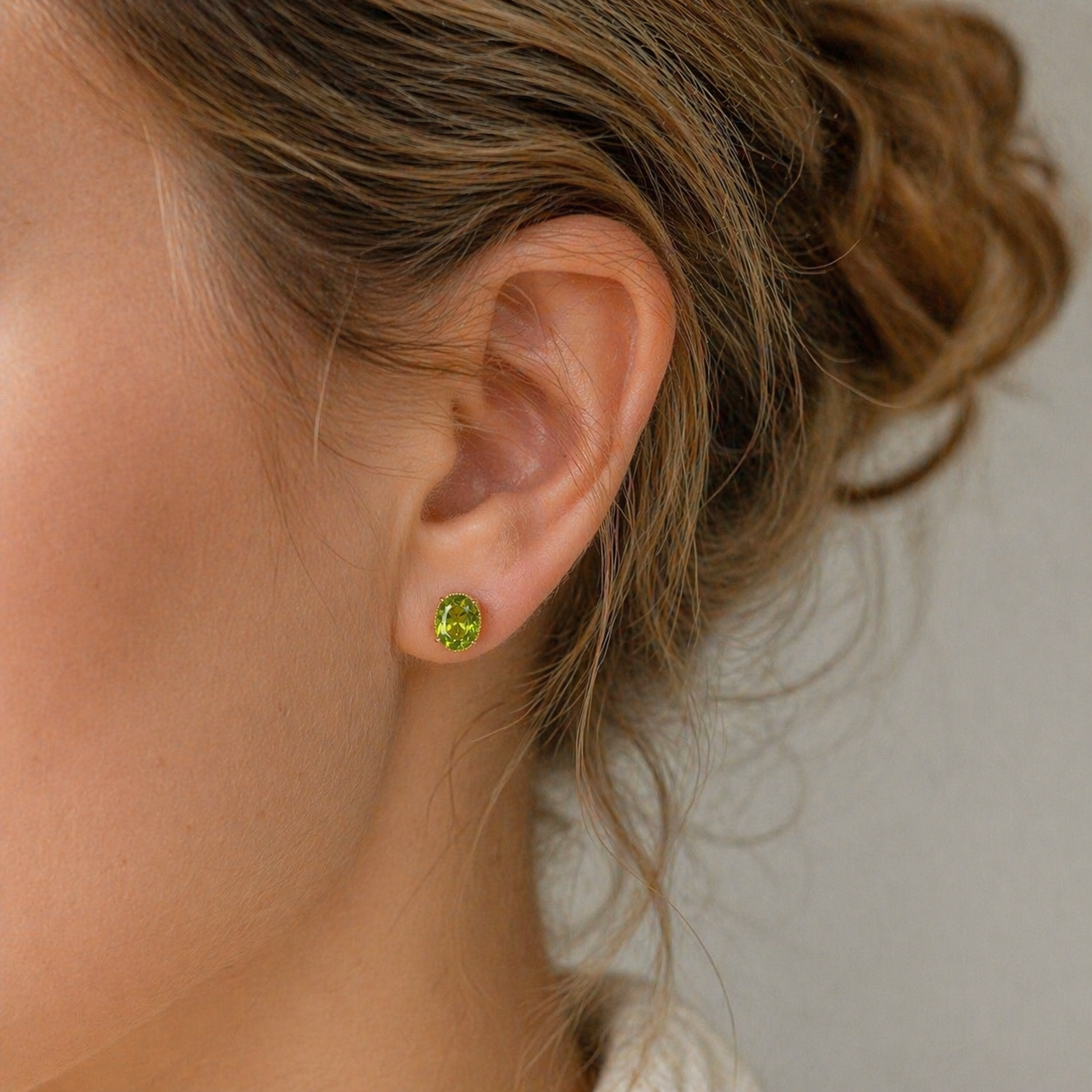 Close-up of an ear wearing a green peridot stud earring with blurred background