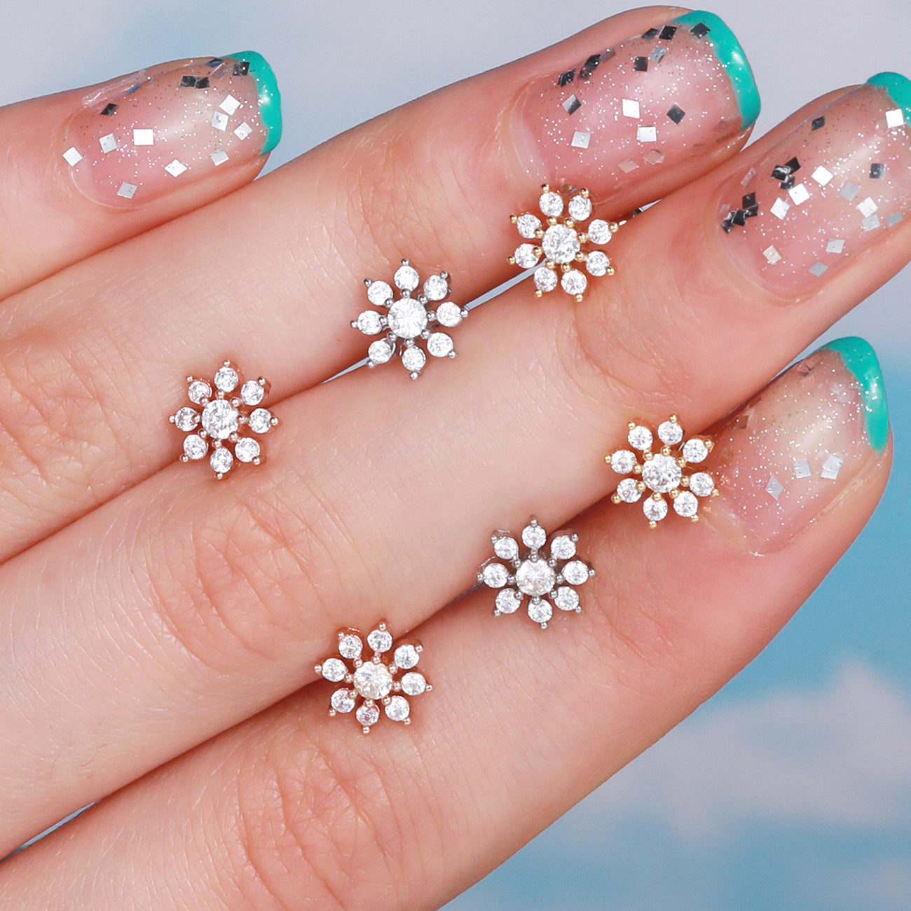 Rose gold and white gold cubic zirconia cartilage earrings in floral design held by hand with manicured nails.