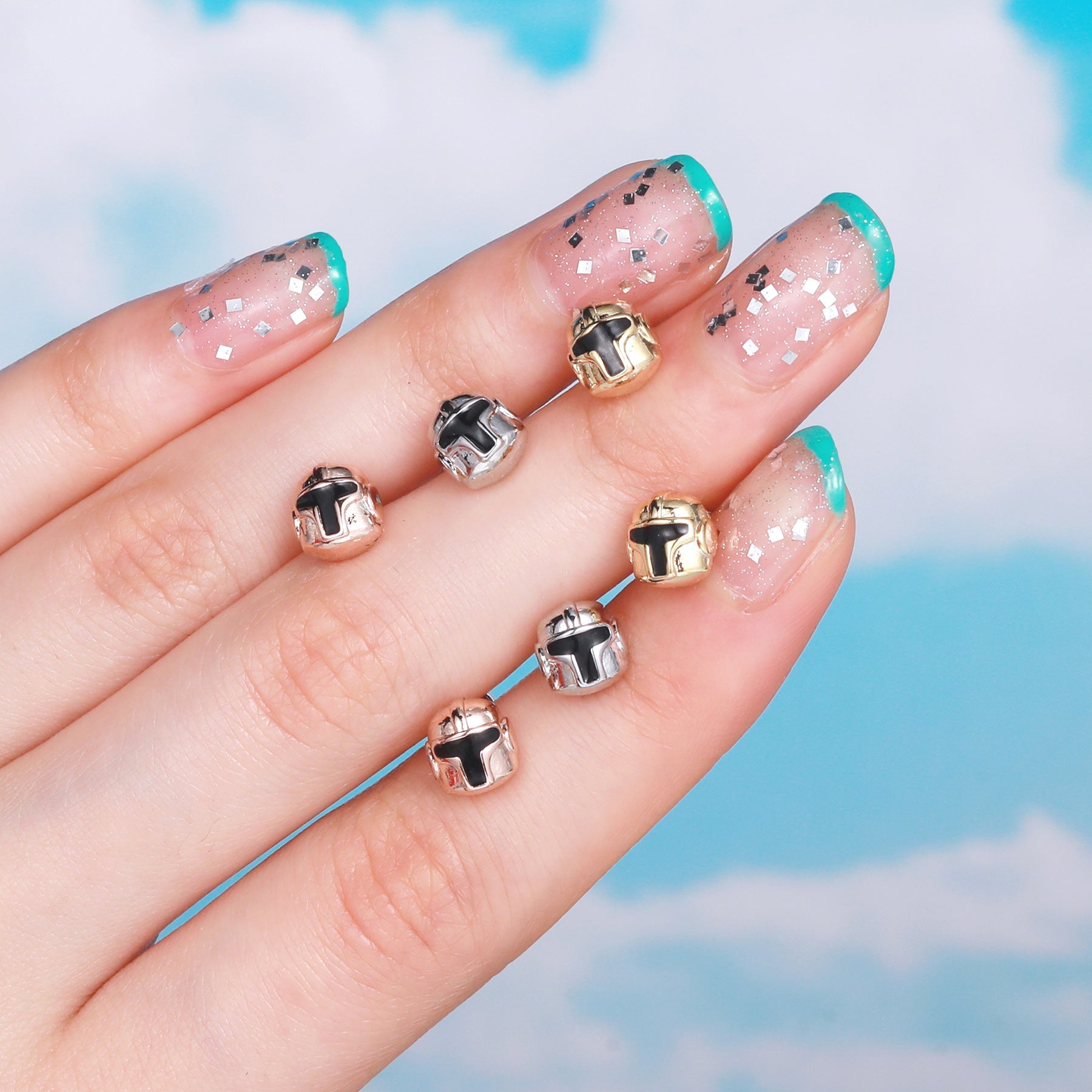 20G rose gold cartilage tiny stud emoji tragus piercings displayed on a hand with glittery nail polish.