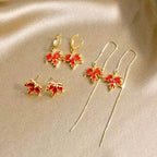 Set of gold earrings with orange maple leaf threader earrings, stud earrings and hoop earrings on a beige background