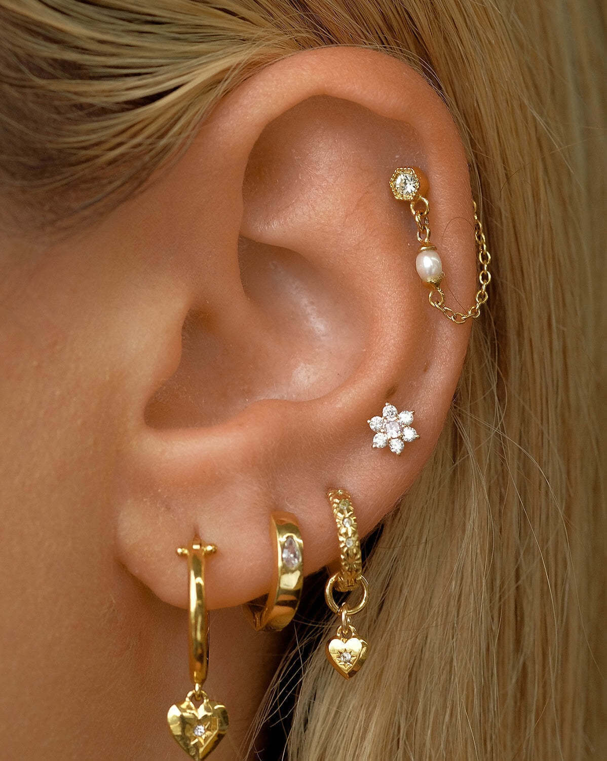 Woman wearing 14K gold floral birthstone cartilage earrings, displaying helix and daith piercings with elegant gold jewelry.