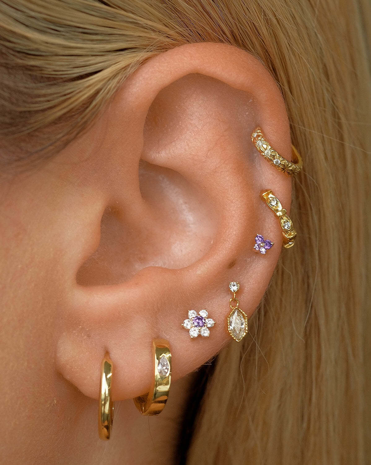 Close-up of ear with 14K gold floral birthstone cartilage earrings, including helix and daith earrings for a stylish and elegant look.