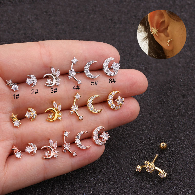 A collection of small cartilage conch stud earrings in various designs, including moons and stars, held in a hand. The earrings are in gold, silver, and rose gold colors.