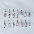 A set of silver belly rings with various embellishments, including a heart-shaped dangle, displayed on a flat surface.