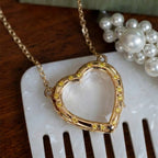 Gold heart-shaped necklace with embedded stones on a white surface