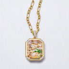 Gold necklace with a pendant featuring a scenic design on a light gray background