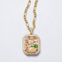 Gold necklace with a pendant featuring a scenic design on a light gray background
