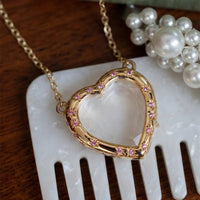 Gold heart-shaped necklace with pink stones on a white comb